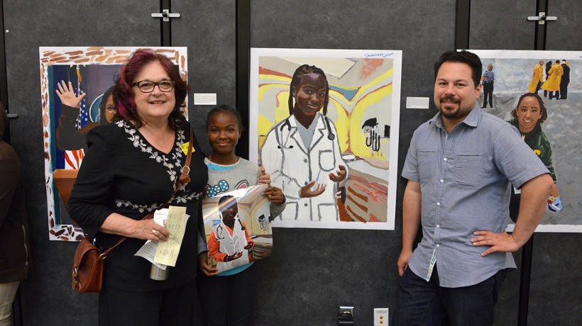 Judy Baca and Carlos Rogel with 6th grade student, Shatairah Wilson in front of her completed self-portrait.